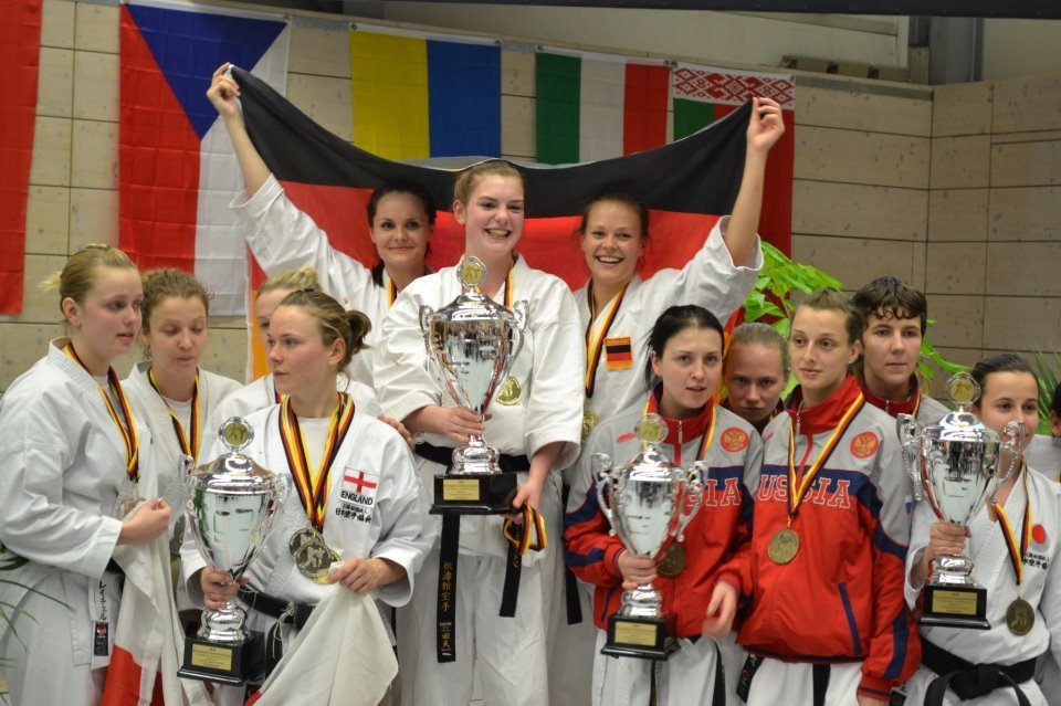 Karatekas mit Pokalen und Medaillen bei der Europameisterschaft, im Hintergrund eine Deutschlandfahne