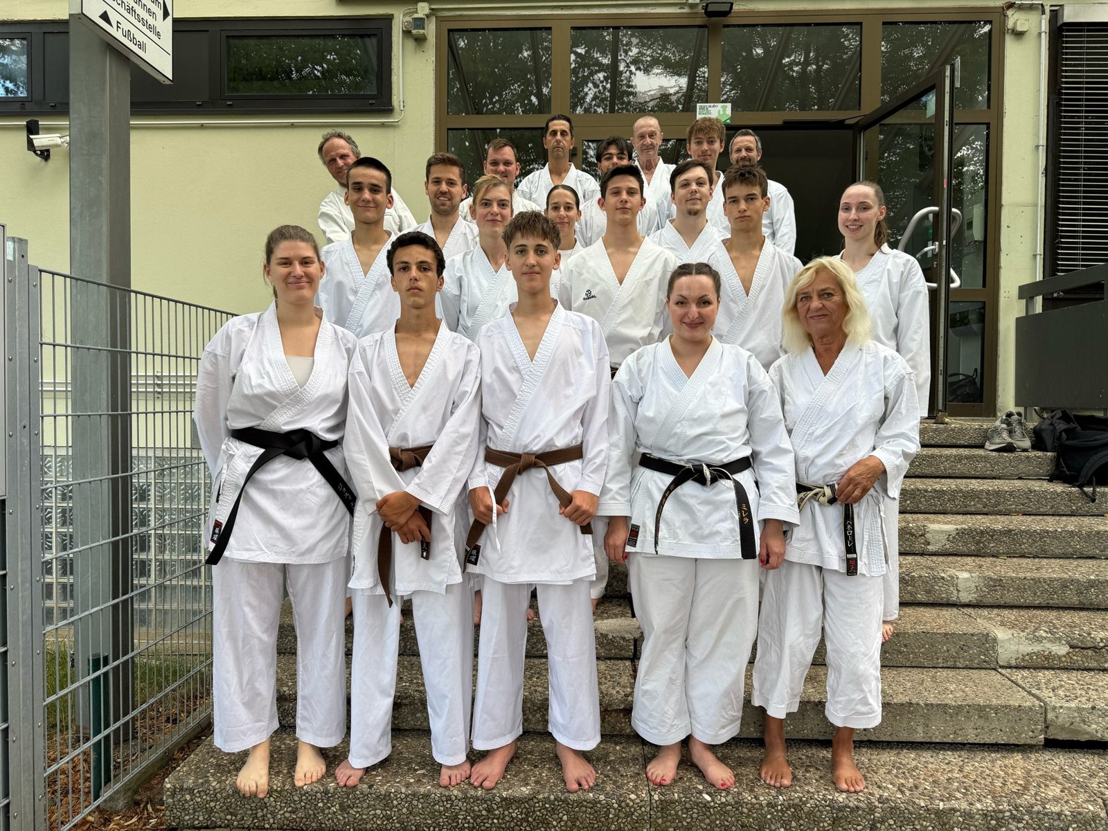 Gruppenfoto von Karatekas in weißen Anzügen auf einer Treppe vor der Sporthalle